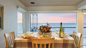 A dining table set with plates, glasses, and a bottle, overlooking the sea. - Oceanfront La Selva Beach Home w/ Fireplace, Views & Direct Beach Access Sand Castle by Avantstay (Watsonville)
