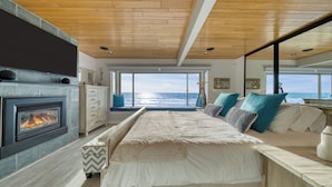A bedroom with a fireplace, a bed with pillows, a view of the ocean, and a wooden ceiling. - Oceanfront La Selva Beach Home w/ Fireplace, Views & Direct Beach Access Sand Castle by Avantstay (Watsonville)
