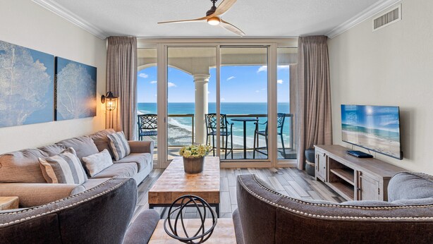 Een ruime woonkamer met balkon en uitzicht op zee, met een bank, salontafel en televisie.