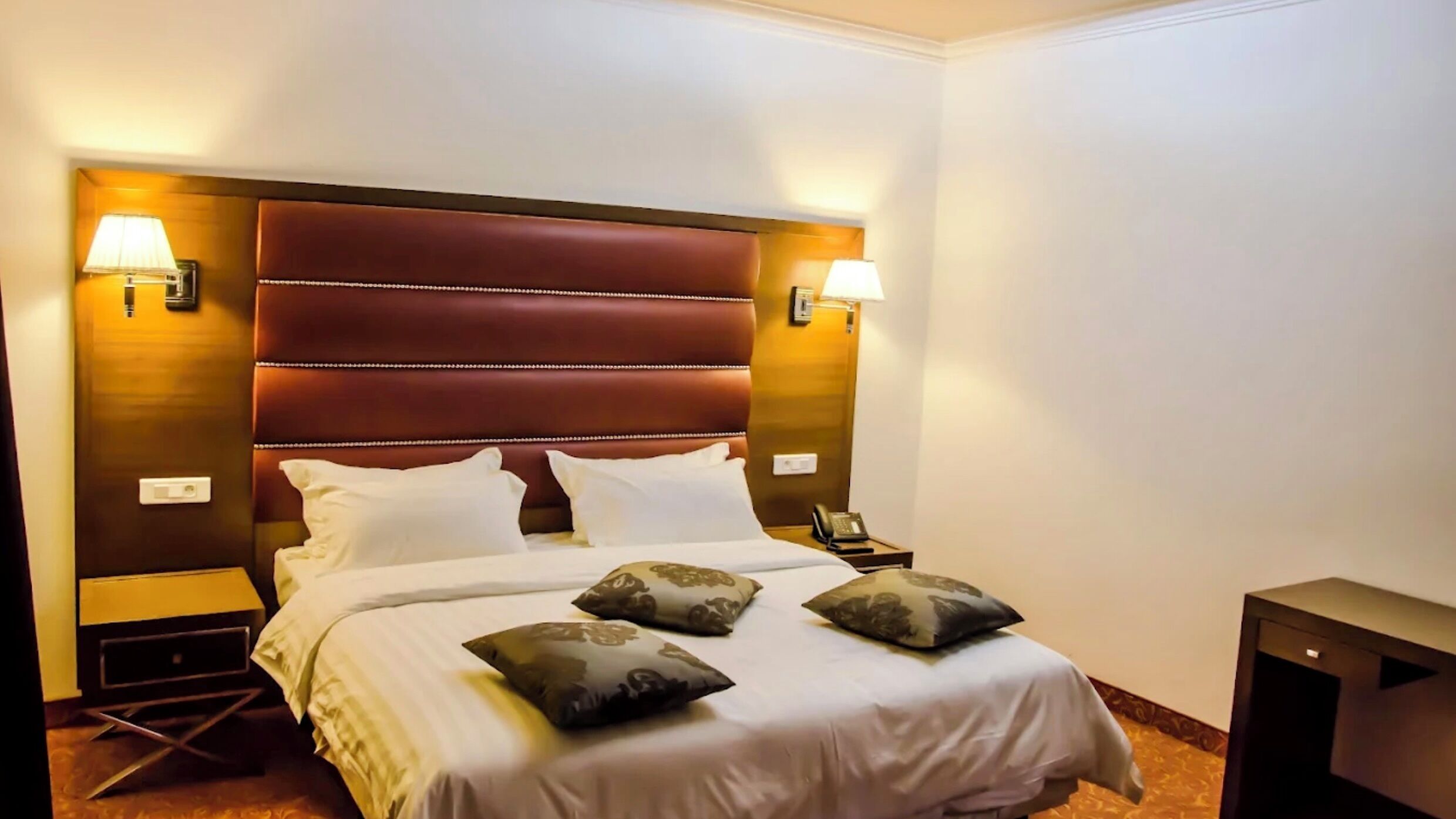 A hotel room with a large bed, two bedside lamps, a nightstand, and a small table.