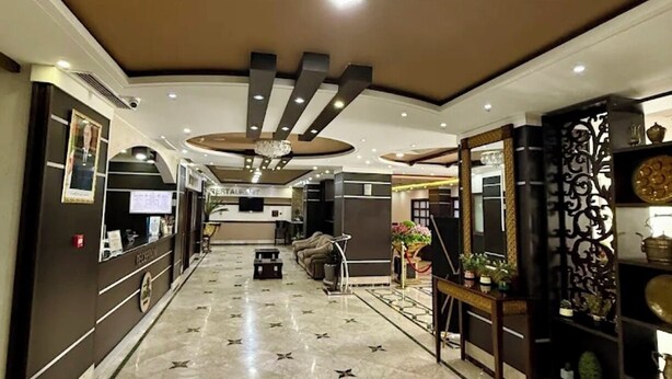 Un hall de hotel con mostrador de recepción, zona de estar y techo decorativo.