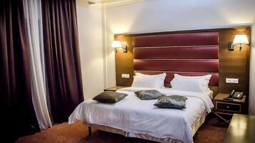 A hotel room with a large bed, two bedside lamps, a nightstand, and a window with curtains.