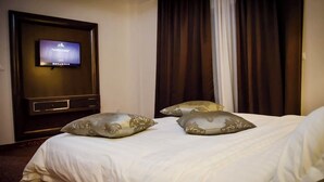 Una habitación de hotel con una cama, un televisor montado en la pared y una ventana con cortinas.