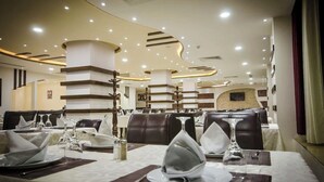 Un restaurante con una decoración moderna, que presenta asientos escalonados y una columna central. Las mesas están dispuestas con manteles blancos, platos y cubiertos.
