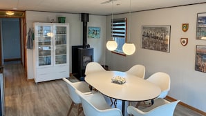 Un coin repas avec une table ronde, des chaises blanches, un meuble vitré et un poêle à bois.