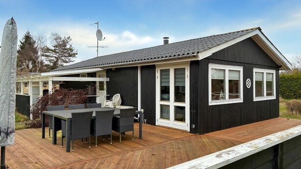 Une maison moderne dotée d’une terrasse en bois, d’un coin repas avec mobilier d’extérieur et d’une antenne parabolique.
