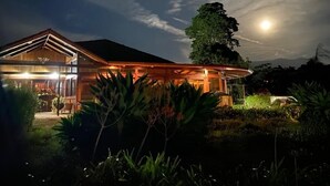 Uma casa moderna com um alpendre espaçoso e um jardim iluminado à noite.