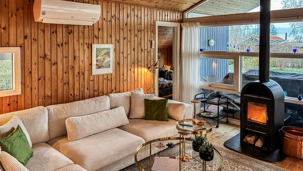 A cozy living room with a wooden wall, a sofa, a coffee table, and a wood-burning stove. - Nice home in Rødvig Stevns with WiFi (Rødvig Stevns)