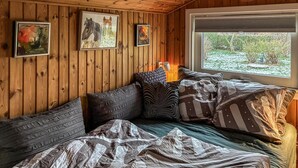 A cozy room with wooden walls, a bed with patterned bedding, and artwork on the walls. - Nice home in Rødvig Stevns with WiFi (Rødvig Stevns)