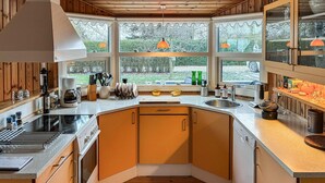 A modern kitchen with wooden cabinets, a built-in oven, a coffee maker, and a large window offering a view of the outdoors. - Nice home in Rødvig Stevns with WiFi (Rødvig Stevns)