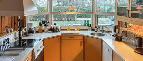 A modern kitchen with wooden cabinets, a built-in oven, a coffee maker, and a large window offering a view of the outdoors.
