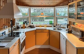 A modern kitchen with wooden cabinets, a built-in oven, a coffee maker, and a large window offering a view of the outdoors. - Nice home in Rødvig Stevns with WiFi (Rødvig Stevns)