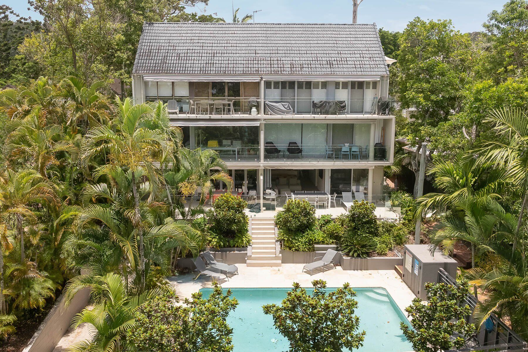 A two-story building with a swimming pool, surrounded by lush greenery.