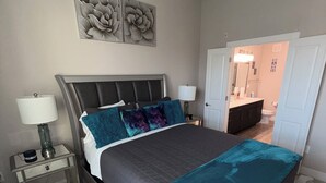 Un dormitorio con cama, mesitas de noche, lámpara y una puerta que da al baño.