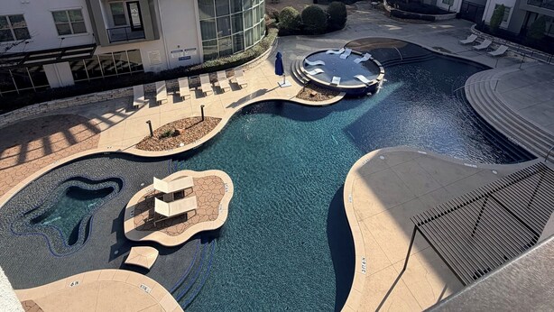 Un moderno complejo de apartamentos con piscina central, mobiliario exterior y un jacuzzi circular.
