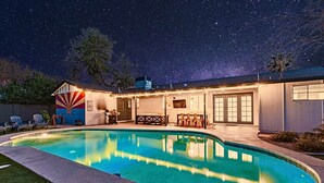 Uma piscina com borda curva, um espaço coberto com mobiliário de exterior e um céu estrelado.