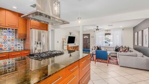 Uma cozinha moderna com ilha central, eletrodomésticos de aço inoxidável e área de refeições com sofá e cadeiras.