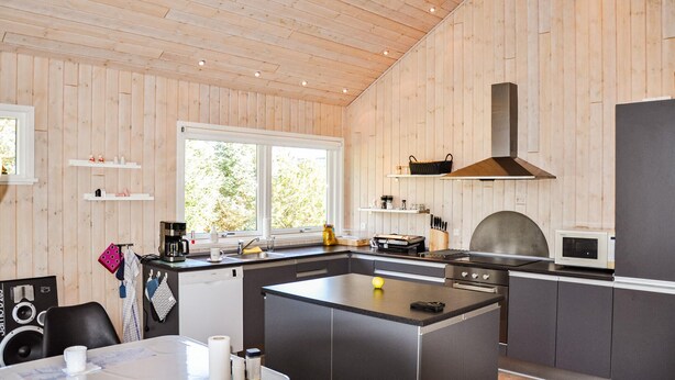 A modern kitchen with wooden walls, a central island, and built-in appliances. - Gorgeous home in Tarm with sauna (Tarm)