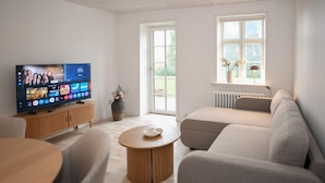 Ein modernes Wohnzimmer mit Flachbildfernseher, Holzschrank, rundem Couchtisch und grauem Sofa.