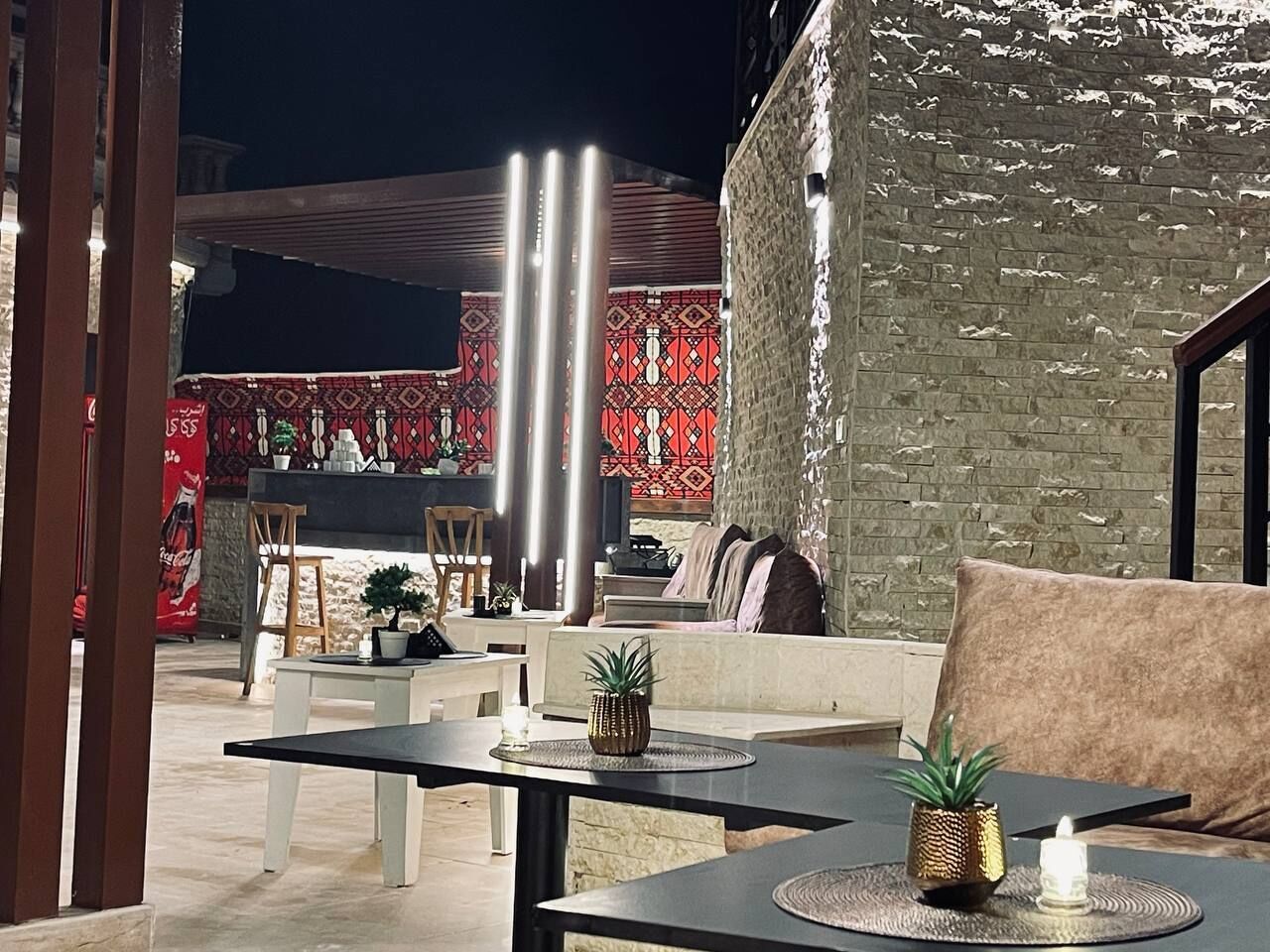 An outdoor seating area with tables and chairs, a brick wall, and a patterned wall in the background.