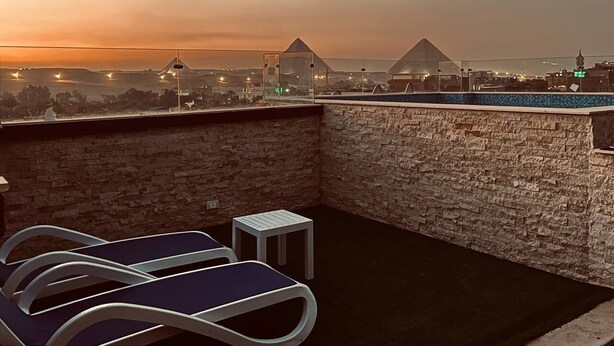 A rooftop terrace with lounge chairs and a small table, overlooking a cityscape at sunset. - MARQUIS PYRAMIDS HOTEL (Giza)