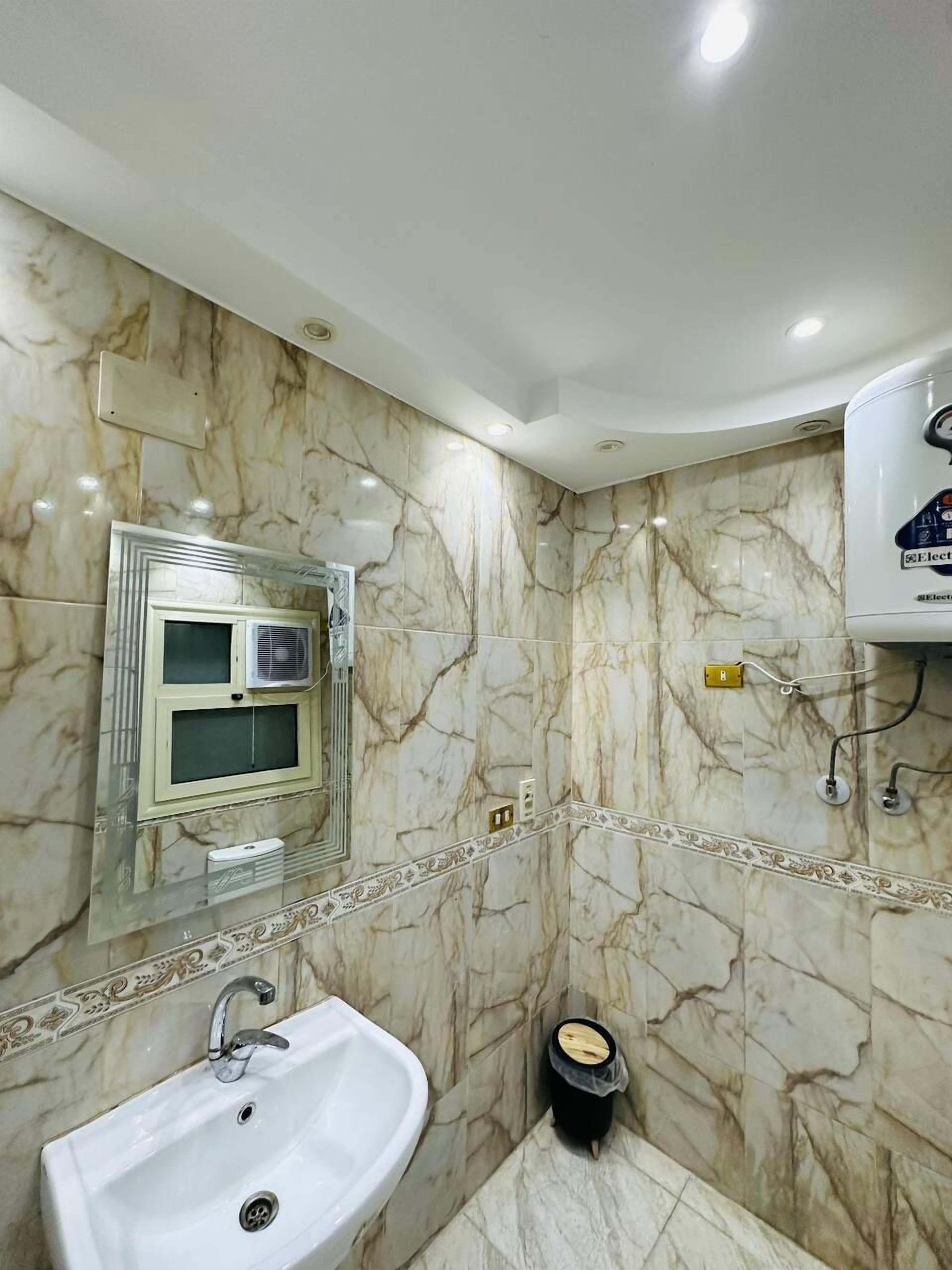 Een badkamer met een marmeren wand, een wastafel, een spiegel en een aan het plafond bevestigde airconditioner.
