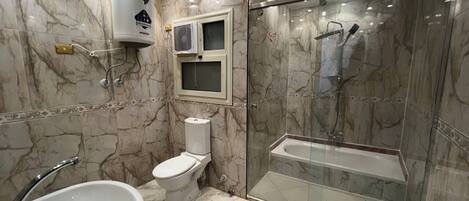 Une salle de bain avec un sol en marbre, un lavabo blanc, des toilettes, une douche en verre et une fenêtre intégrée au mur.