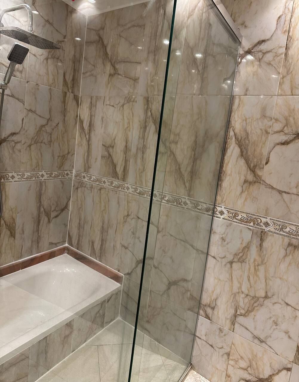 A modern bathroom with marble walls, a glass shower enclosure, and a white sink.