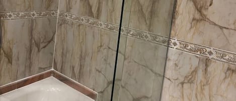 A modern bathroom with marble walls, a glass shower enclosure, and a white sink.