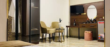 A hotel room with a bed, a seating area with two chairs, a desk with a mirror, and a wardrobe.