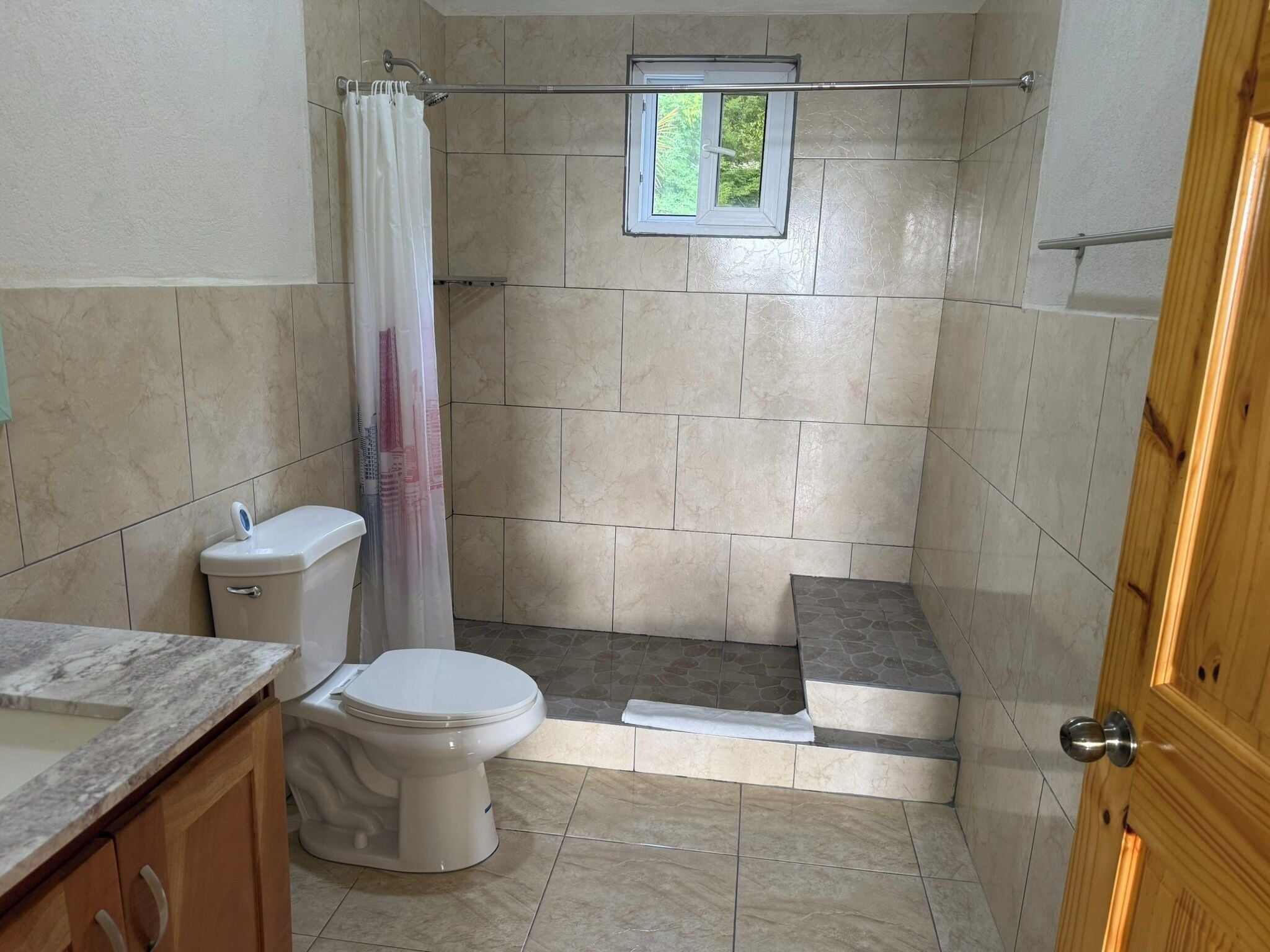 Un bagno con il water, doccia e una piccola finestra.