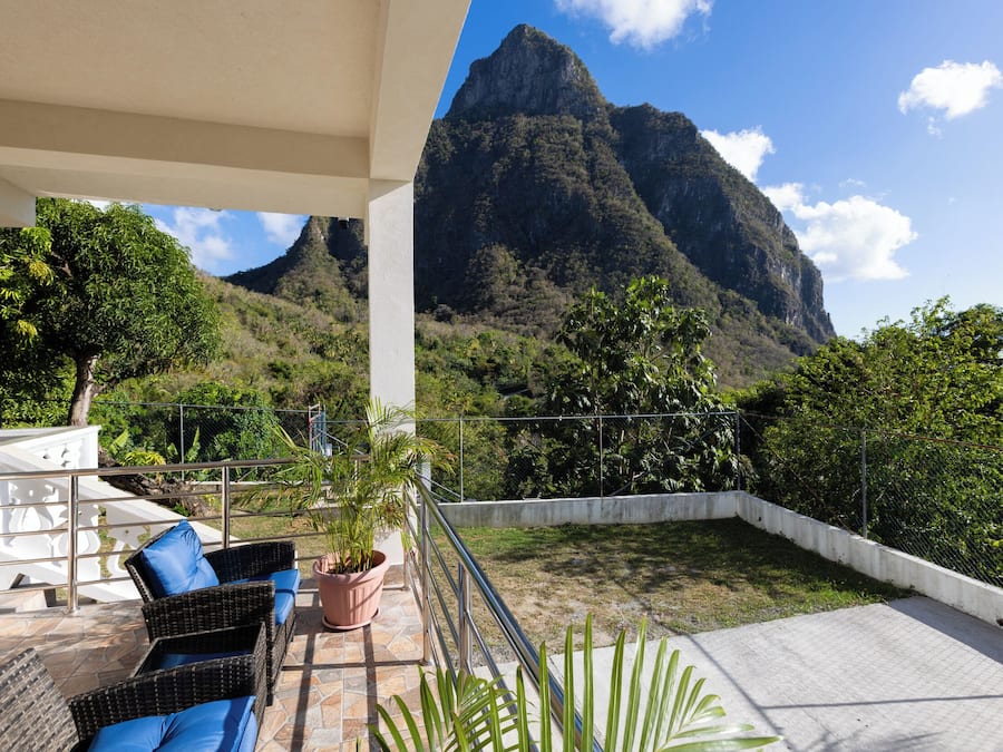 Un balcón con mobiliario de mimbre y una planta en maceta, con vistas a un paisaje montañoso.