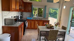 A kitchen with wooden cabinets, a stove, and a dining area with wicker chairs and a table. - You 4 Ric Piton Suites (Soufriere)