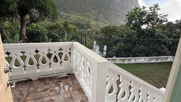 A balcony with a stone-tiled floor and white decorative railings, overlooking a mountainous landscape.
