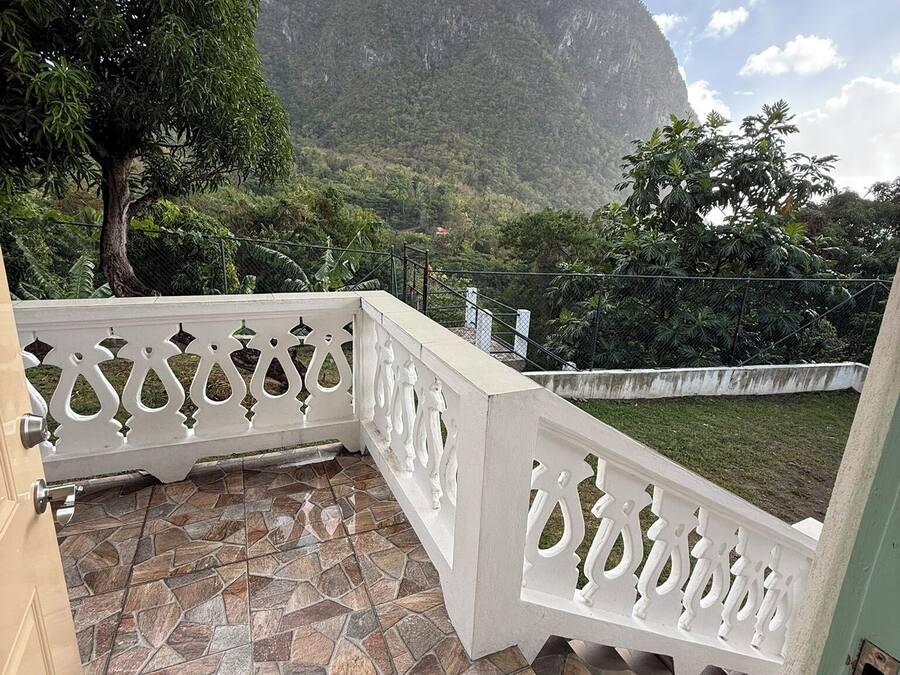 A balcony with a stone-tiled floor and white decorative railings, overlooking a mountainous landscape.