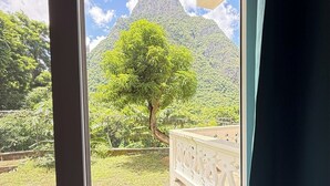 A window with a view of a lush garden, a tree, and a mountain. - You 4 Ric Piton Suites (Soufriere)