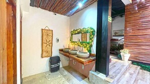 Une salle de bain avec un meuble-lavabo en bois, trois vasques en céramique, un miroir décoratif agrémenté de plantes et une petite plante en pot.