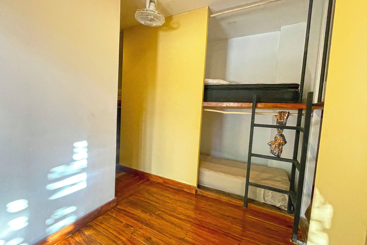 A room with a wooden floor, a bunk bed, a ladder, and a ceiling fan.