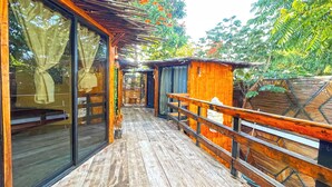 Une terrasse en bois avec des portes vitrées donnant sur une pièce, le tout entouré d’une végétation luxuriante et d’une clôture en bois.