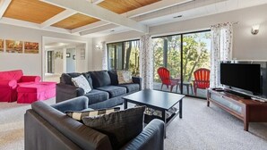 A modern living room with a wooden ceiling, a large TV, and a view of trees through large windows. - Mountain Retreat Near Bryce Resort. Game Rm. Sleeps 8 Family and Dog Friendly! (Basye)