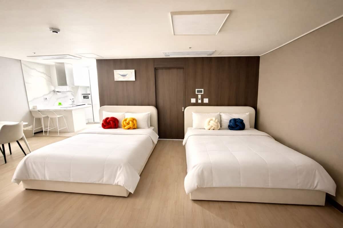 A modern hotel room with two beds, a desk, and a bathroom.