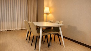Et hotelværelse med et rektangulært spisebord, seks stole, en lampe og et stort vindue med gardiner.