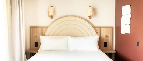 A hotel room with a bed, two bedside tables, a wooden headboard, and a wall-mounted light fixture.