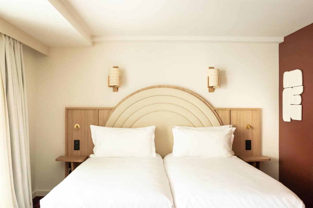 Una cama doble con cabecera de madera, dos mesitas de noche y lámparas de pared.
