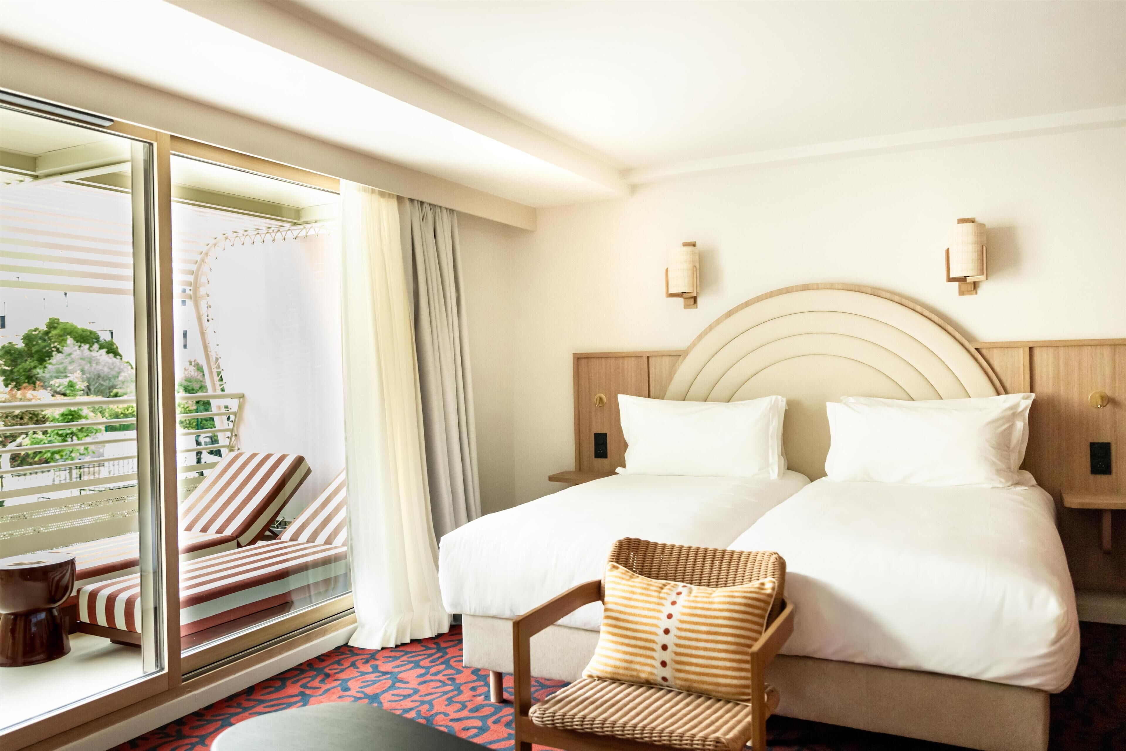 Une chambre d’hôtel avec un grand lit, deux tables de chevet, une chaise, une fenêtre donnant sur un espace verdoyant et un balcon.