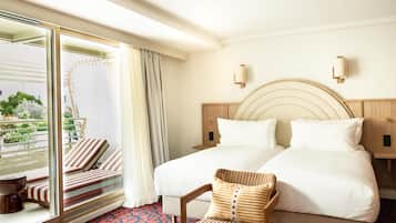 Une chambre d’hôtel avec un grand lit, deux tables de chevet, une chaise, une fenêtre donnant sur un espace verdoyant et un balcon.