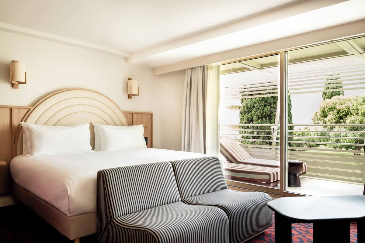 Habitación de hotel con cama, sofá, una mesita y balcón con vistas a zonas verdes.