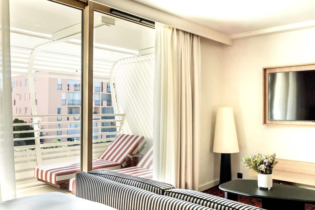 Habitación de hotel con balcón, sofá a rayas, una mesita con lámpara y una planta en maceta.