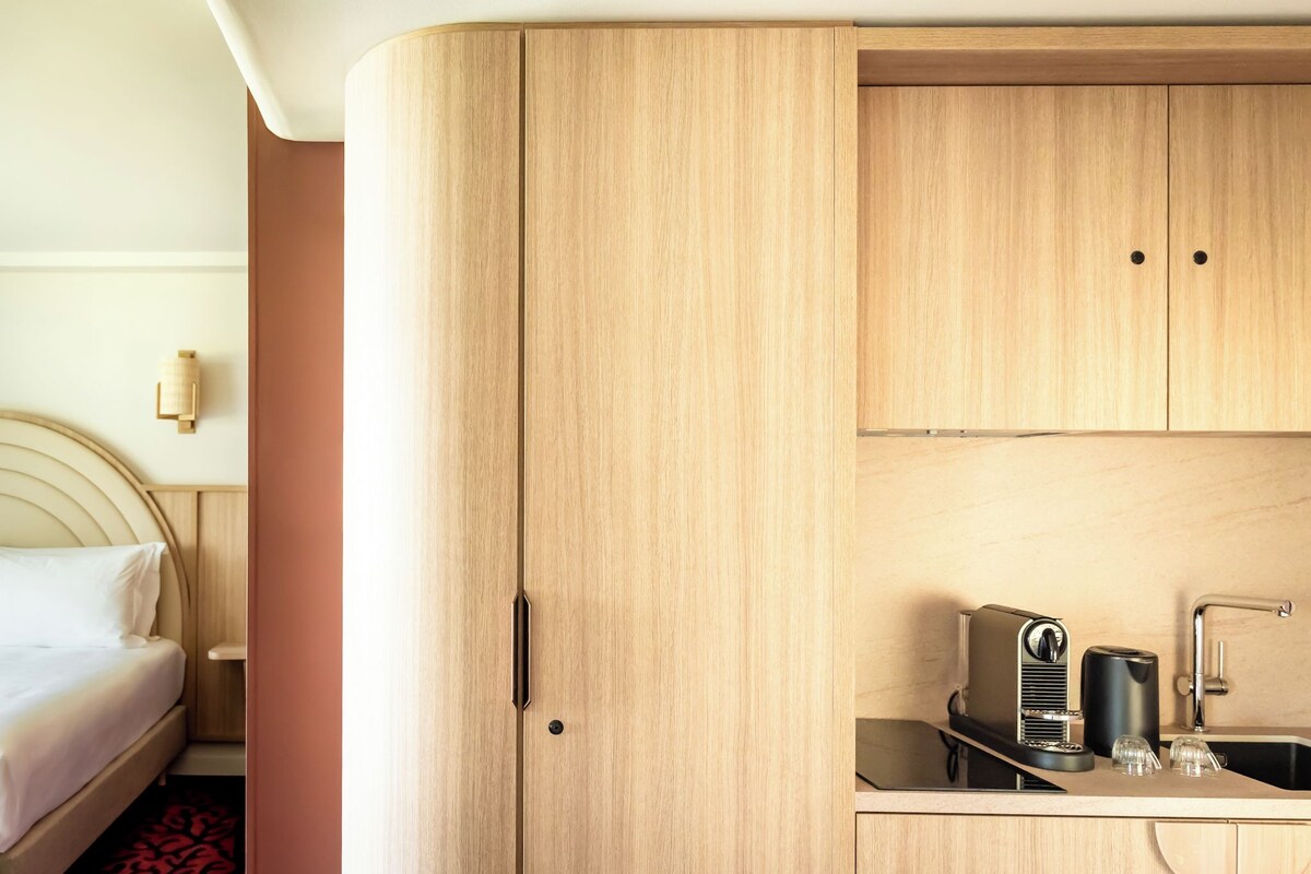 Una habitación de hotel compacta con una cama, una kitchenette con cafetera y un lavabo.