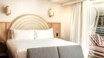 A hotel room with a large bed, a wooden headboard, two wall-mounted light fixtures, a window with curtains, and a striped sofa.